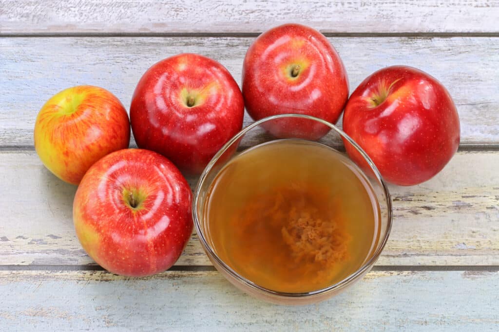 Raw Apple Cider Vinegar (ACV) with Mother and Five Apples on Wooden Table