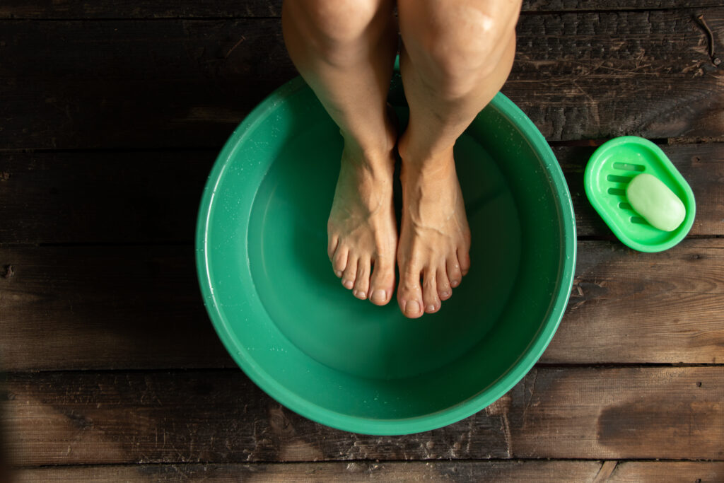 girl washes her feet in a green bowl on the wooden floor of the house, foot care, wash feet
