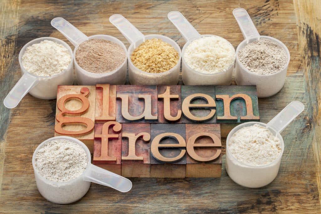 measuring scoops of gluten free flours (almond, coconut, teff, flaxseed meal, whole rice, brown rice, buckwheat) with the word Gluten in letterpress wood type